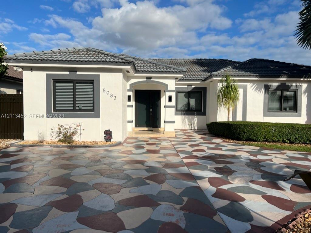 Stucco exterior featuring dark-toned window trim, a multi-colored stone-pattern driveway, a recessed entryway, and a low-profile tile roof