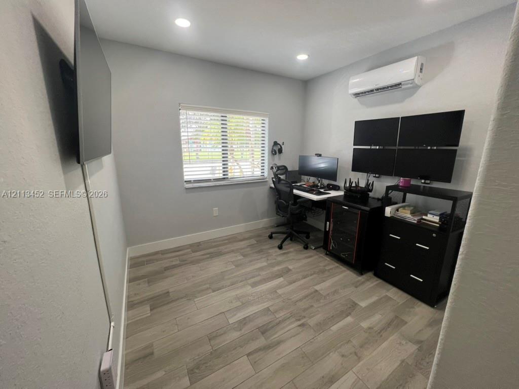 Interior room featuring wood-finish flooring, recessed lighting, a wall-mounted ductless mini-split HVAC unit, and a window with horizontal blinds