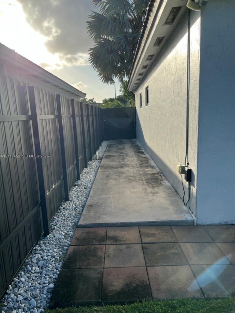 Exterior side path featuring a concrete walkway, decorative stone border, privacy fencing, and paved patio section