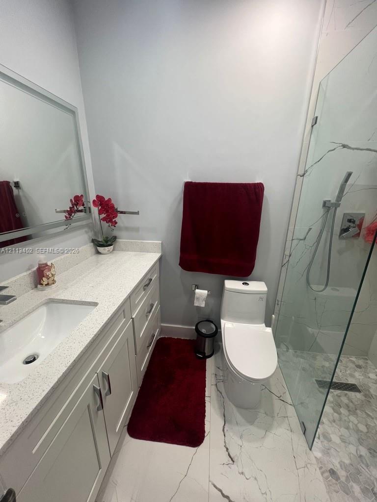 Bathroom featuring a vanity with a light-toned countertop, integrated rectangular sink, framed mirror, and a walk-in shower enclosed by a glass panel with large-format tile flooring
