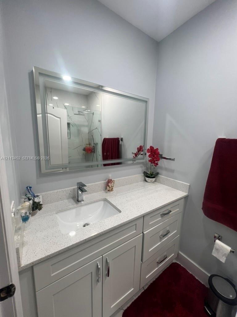 Bathroom vanity featuring light-toned cabinetry, a speckled stone countertop, integrated rectangular undermount sink, chrome faucet, and a large rectangular mirror with an integrated light frame