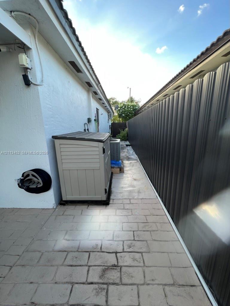 Side yard featuring light-toned concrete paver hardscaping and a tall dark-finished corrugated metal privacy fence