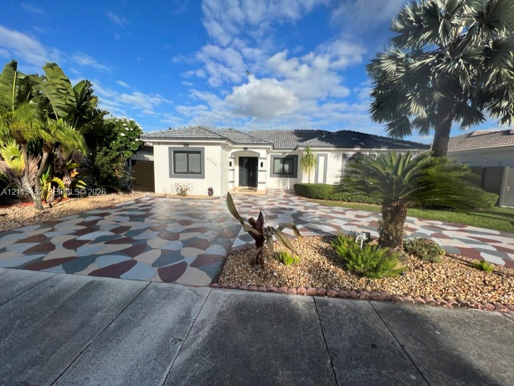 Exterior facade featuring a concrete tile roof, custom-patterned driveway, and manicured landscaping with mature palm trees