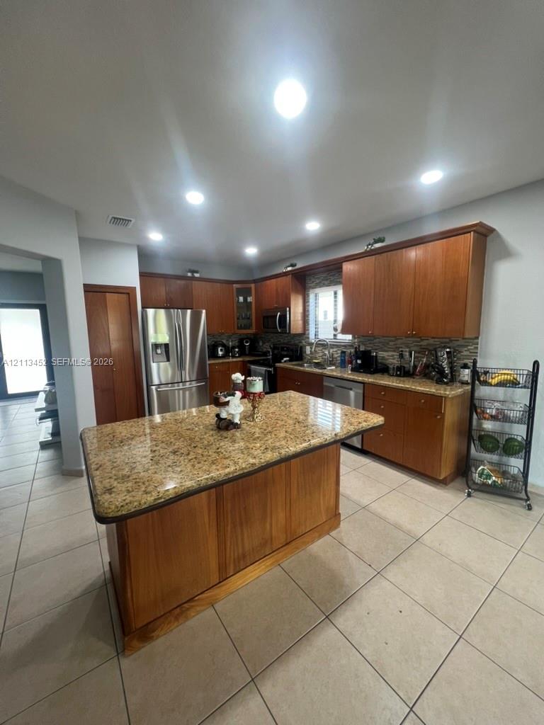 Kitchen featuring a center island, stone-finish countertops, wood-finish cabinetry, stainless steel appliances, and recessed lighting
