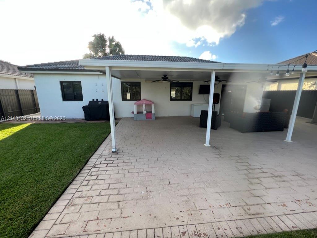 Covered patio featuring paver flooring, ceiling fans, and a spacious backyard with a lawn