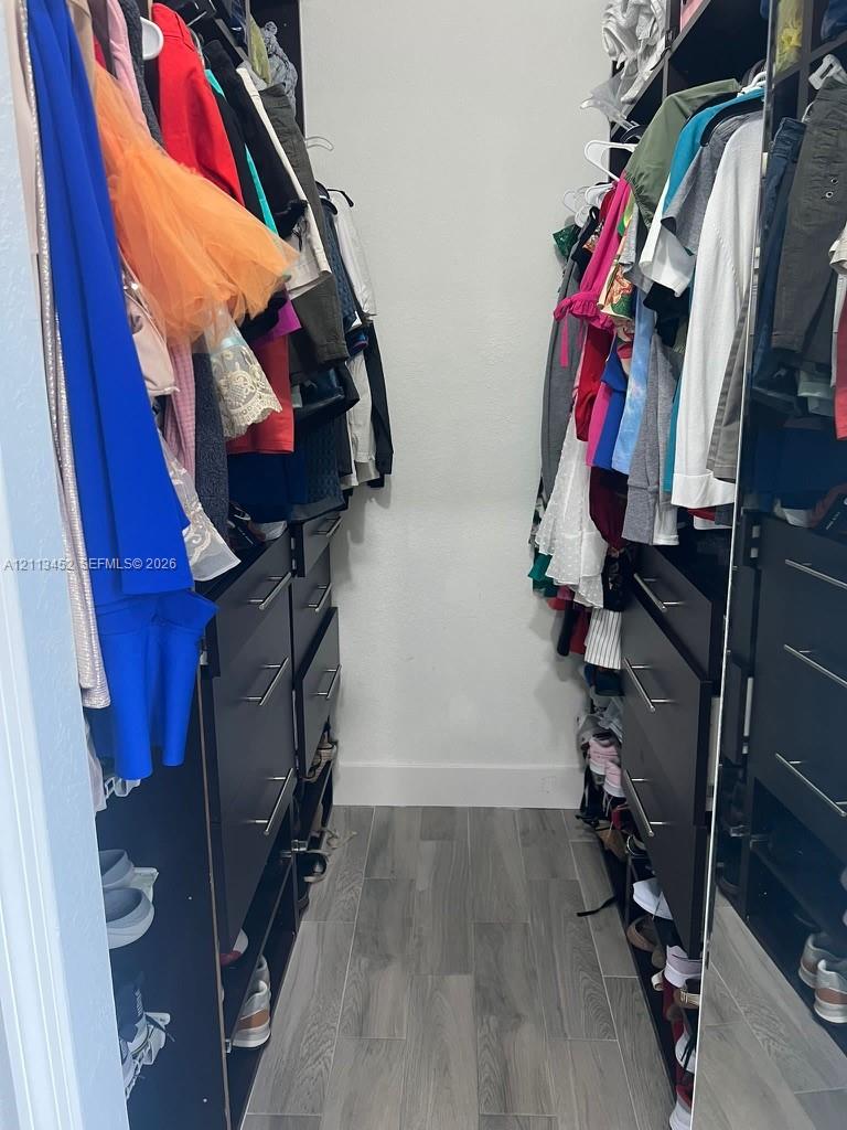 Walk-in closet featuring floor-to-ceiling built-in cabinetry, dark-finish drawers with metallic pulls, open shelving, and wood-finish flooring