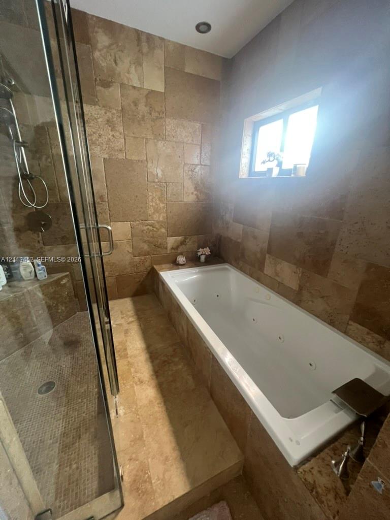 Jetted soaking tub with tile surround, glass-enclosed shower, and natural stone wall and floor tile finishes