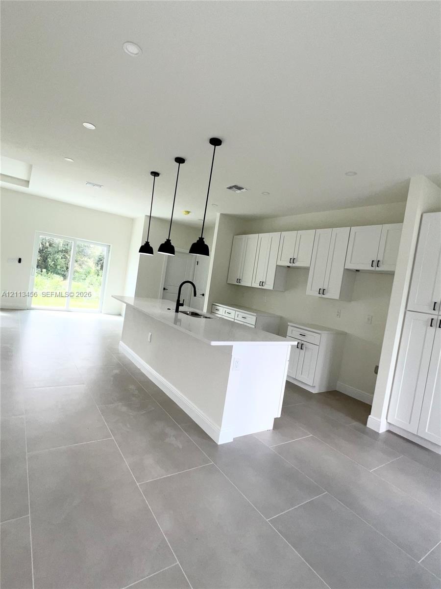 Kitchen featuring white shaker-style cabinetry, quartz countertops, a central island with a matte black faucet, triple pendant lighting, and large-format tile flooring Kitchen featuring white shaker-style cabinetry, quartz countertops, a central island with a matte black faucet, triple pendant lighting, and large-format tile flooring