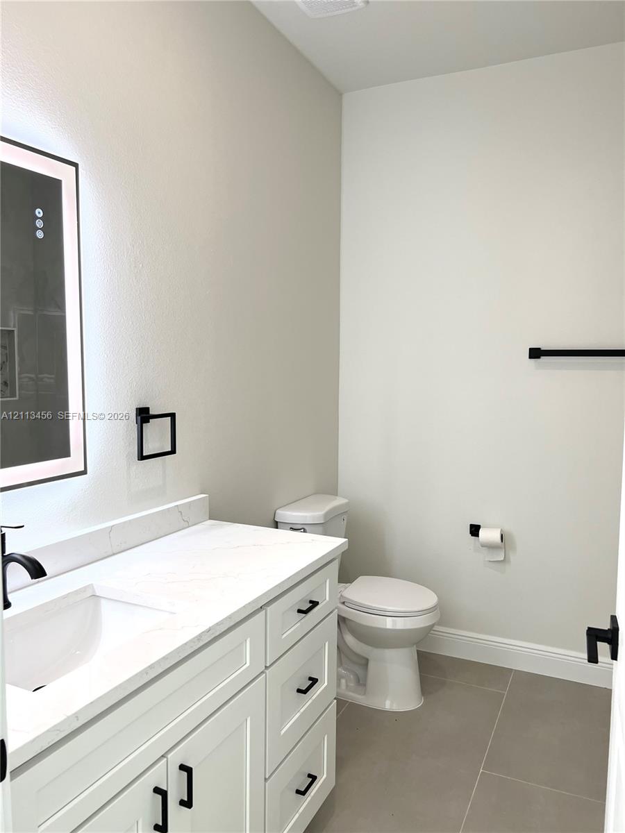 White vanity cabinet featuring a quartz countertop, integrated rectangular sink, matte black hardware, and an illuminated wall-mounted mirror White vanity cabinet featuring a quartz countertop, integrated rectangular sink, matte black hardware, and an illuminated wall-mounted mirror