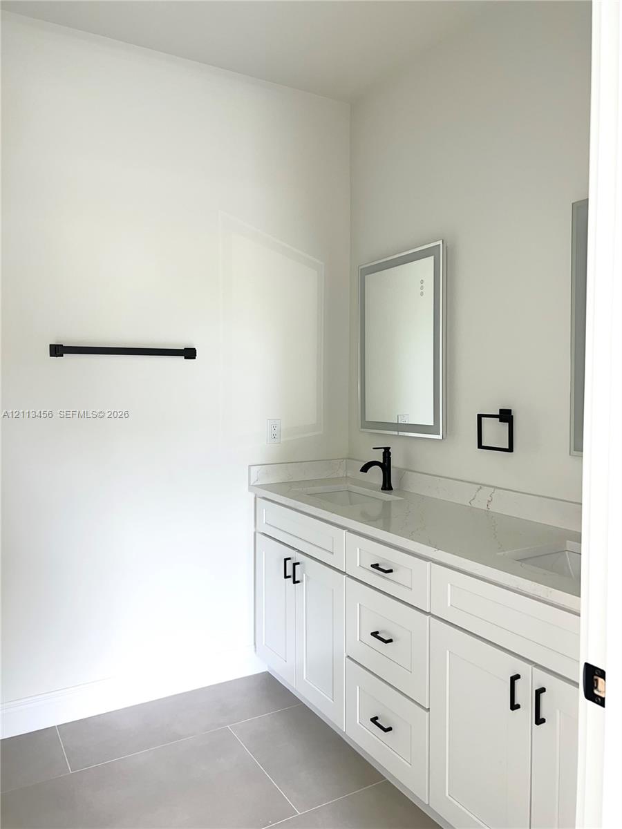 Double-vanity cabinet with white shaker-style doors, stone-composite countertop, dual undermount sinks, matte black fixtures, and integrated mirror lighting Double-vanity cabinet with white shaker-style doors, stone-composite countertop, dual undermount sinks, matte black fixtures, and integrated mirror lighting