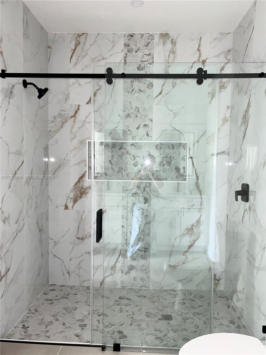 Walk-in shower featuring large-format patterned wall tile, a vertical mosaic accent strip, pebble-stone flooring, a recessed wall niche, and a sliding glass door with matte black hardware Walk-in shower featuring large-format patterned wall tile, a vertical mosaic accent strip, pebble-stone flooring, a recessed wall niche, and a sliding glass door with matte black hardware