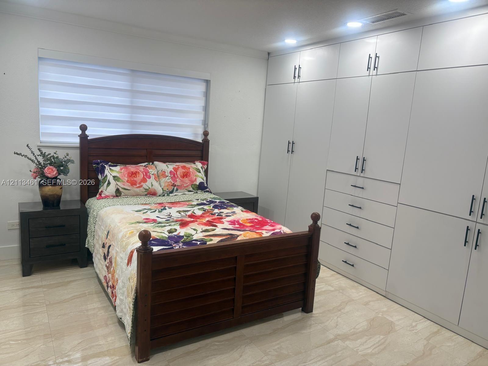 Wall-to-wall built-in cabinetry featuring high-gloss white finish and matte black hardware, recessed ceiling lighting, and large-format tile flooring