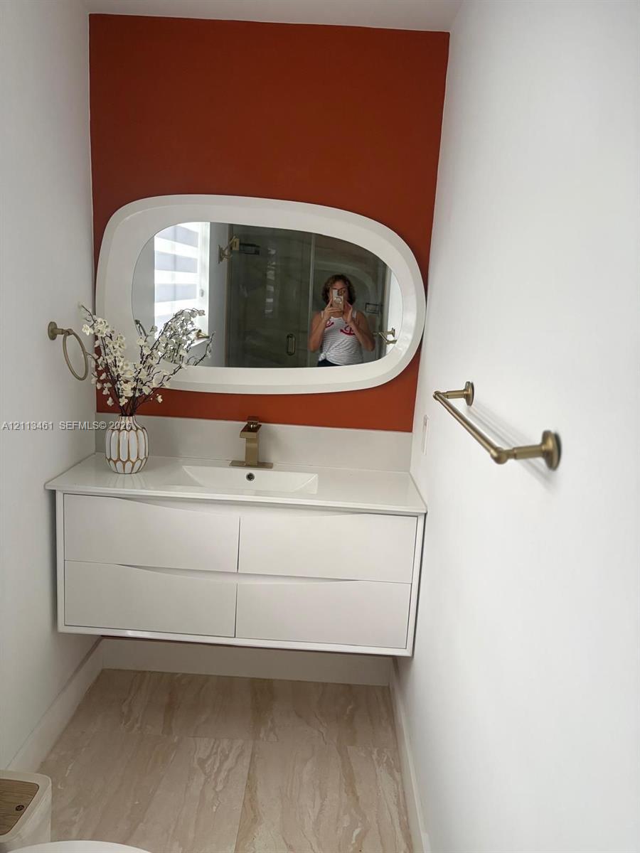 Floating white dual-drawer vanity with an integrated countertop sink, matte gold single-handle faucet, oval-framed mirror, and gold-finish wall-mounted hardware