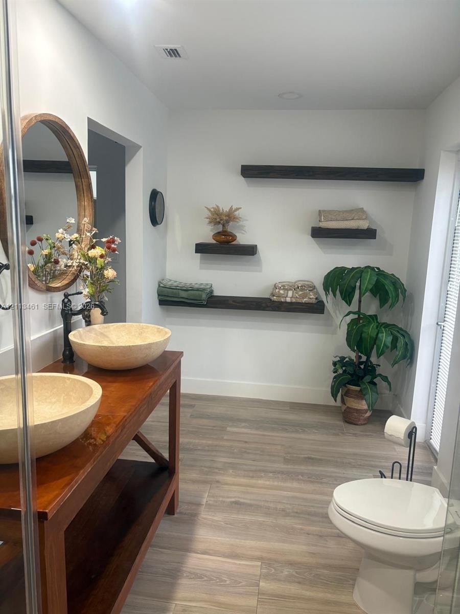 Double-basin vanity with vessel sinks, wood-finish flooring, and floating wall-mounted shelving