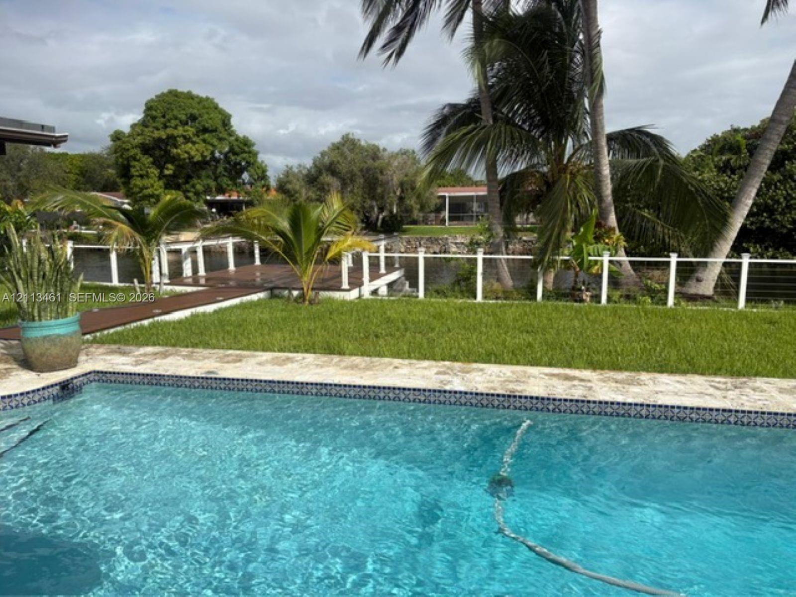 Swimming pool with stone surround, waterfront wooden deck, white railing, and mature landscaping