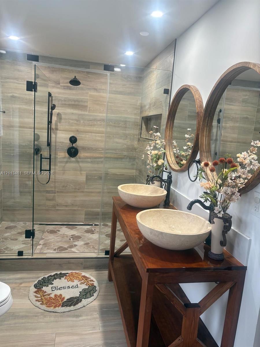 Double vanity featuring natural stone vessel sinks, wooden base cabinetry, and circular framed mirrors, paired with a glass-enclosed shower featuring stone-look tile walls and matte black fixtures