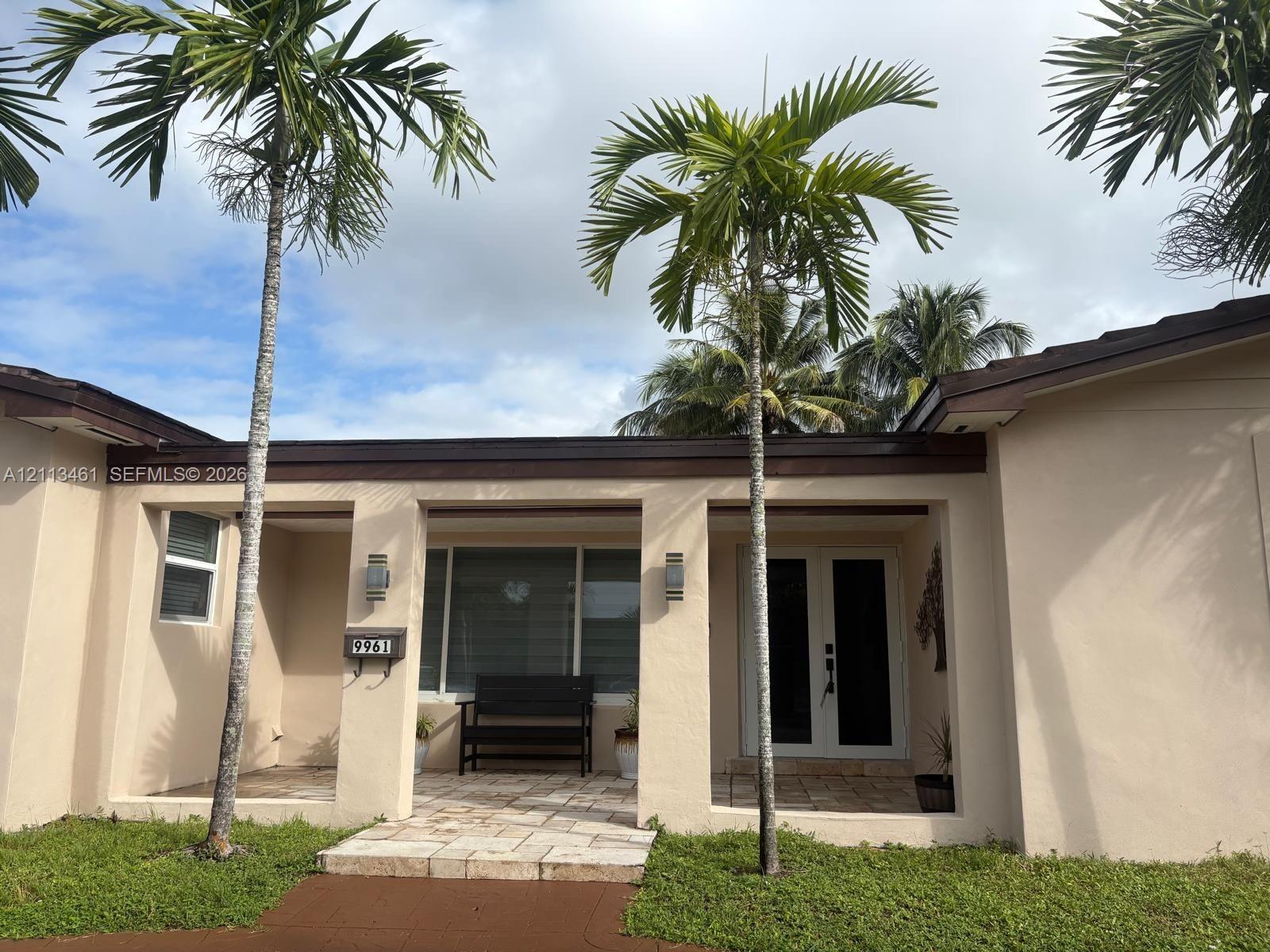 Stucco exterior facade featuring a covered entryway, stone paver porch, dual entry doors, and wall-mounted exterior lighting fixtures