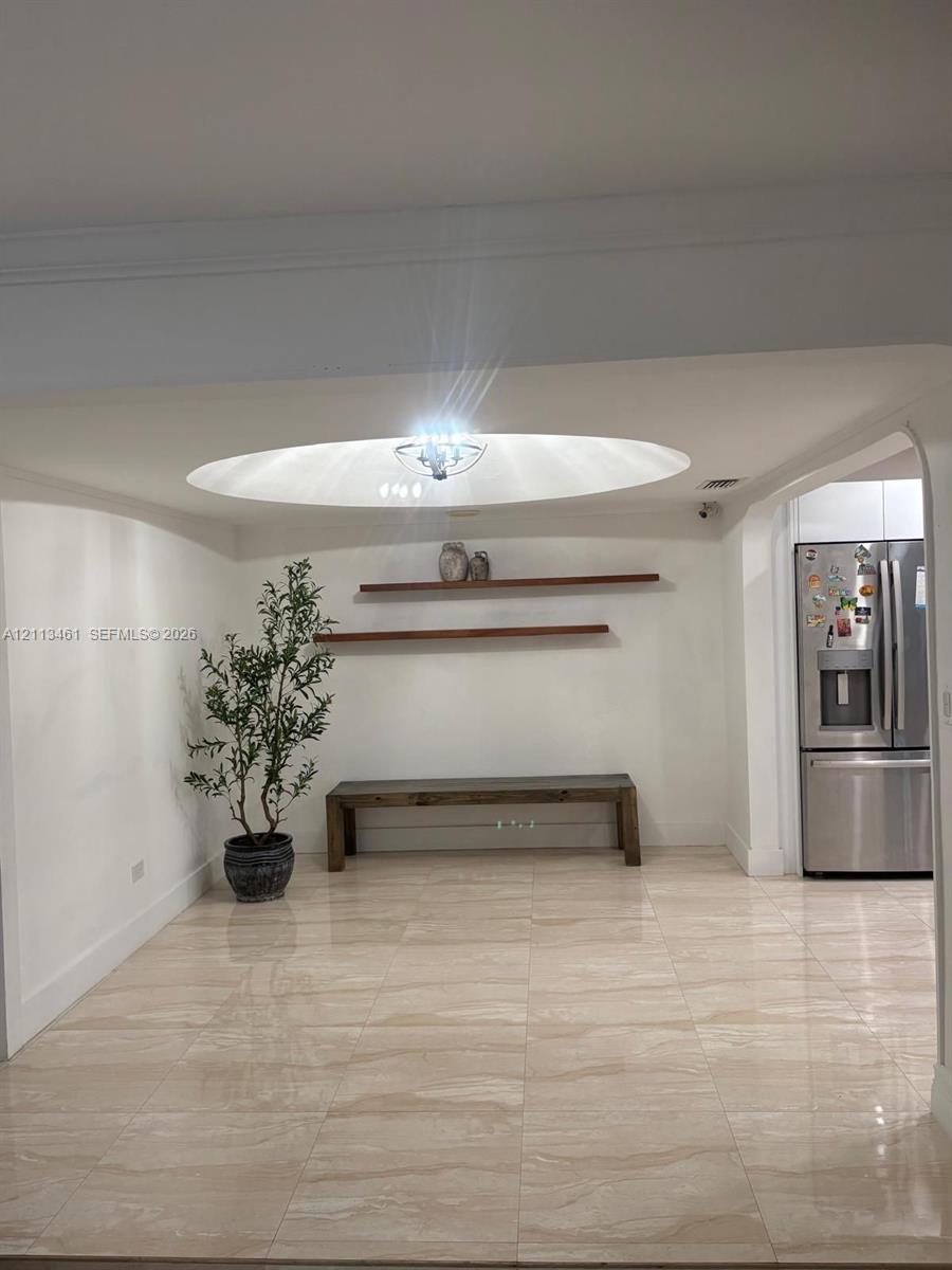 Large-format tile flooring, recessed circular ceiling feature, flush-mount chandelier, and dual wall-mounted floating wood shelves