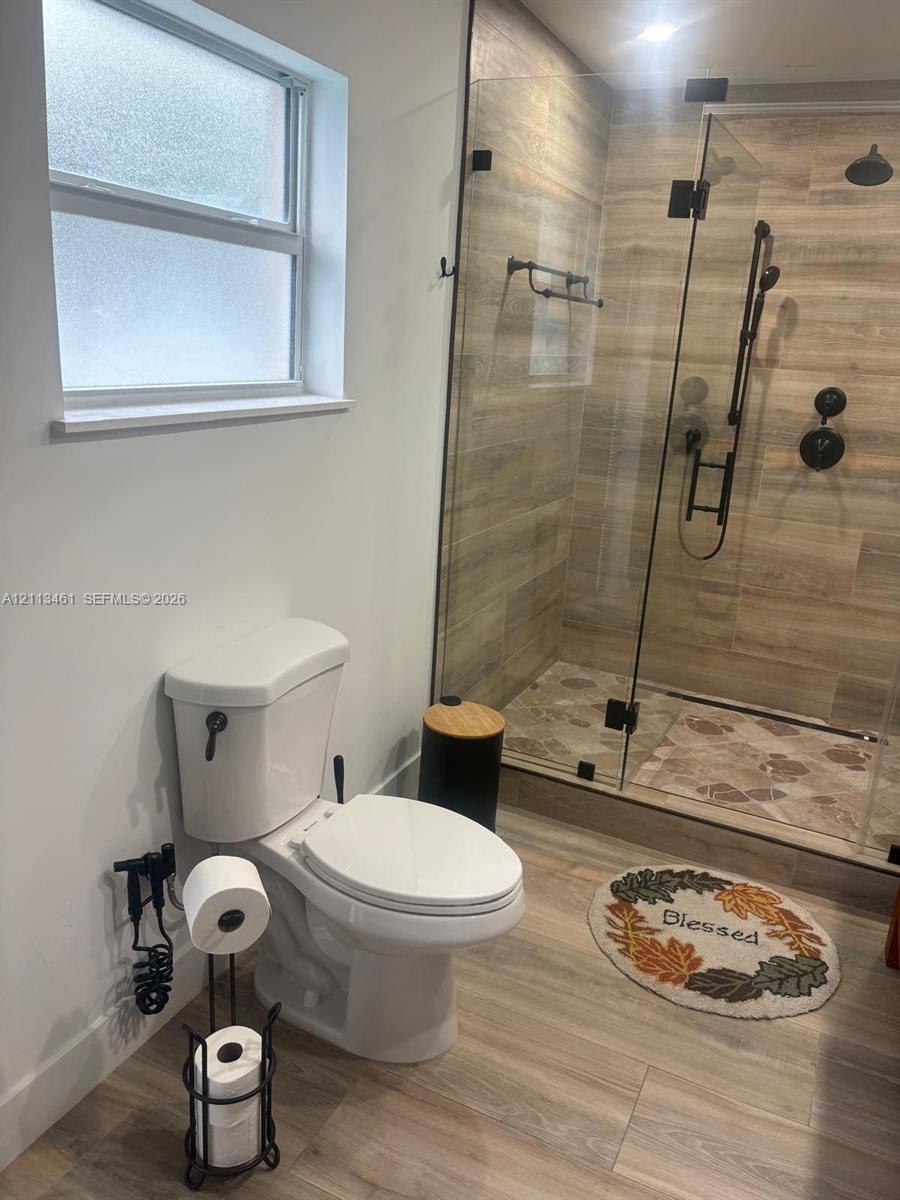Walk-in shower featuring glass enclosure, wood-finish wall tile, and matte black fixtures, paired with wood-finish flooring and privacy-glass window