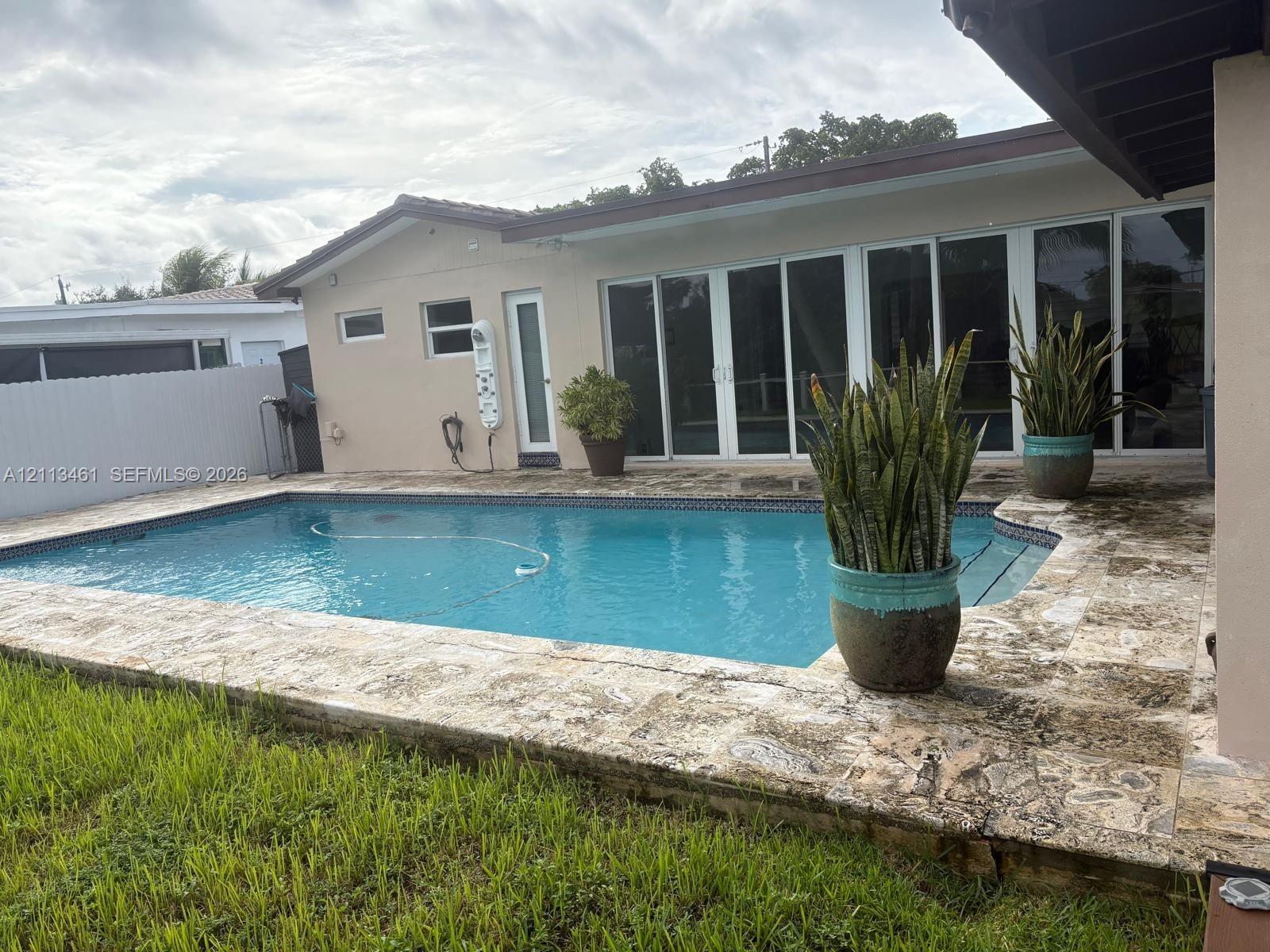 In-ground swimming pool with stone-surfaced deck, white multi-panel sliding glass doors, and perimeter privacy fencing