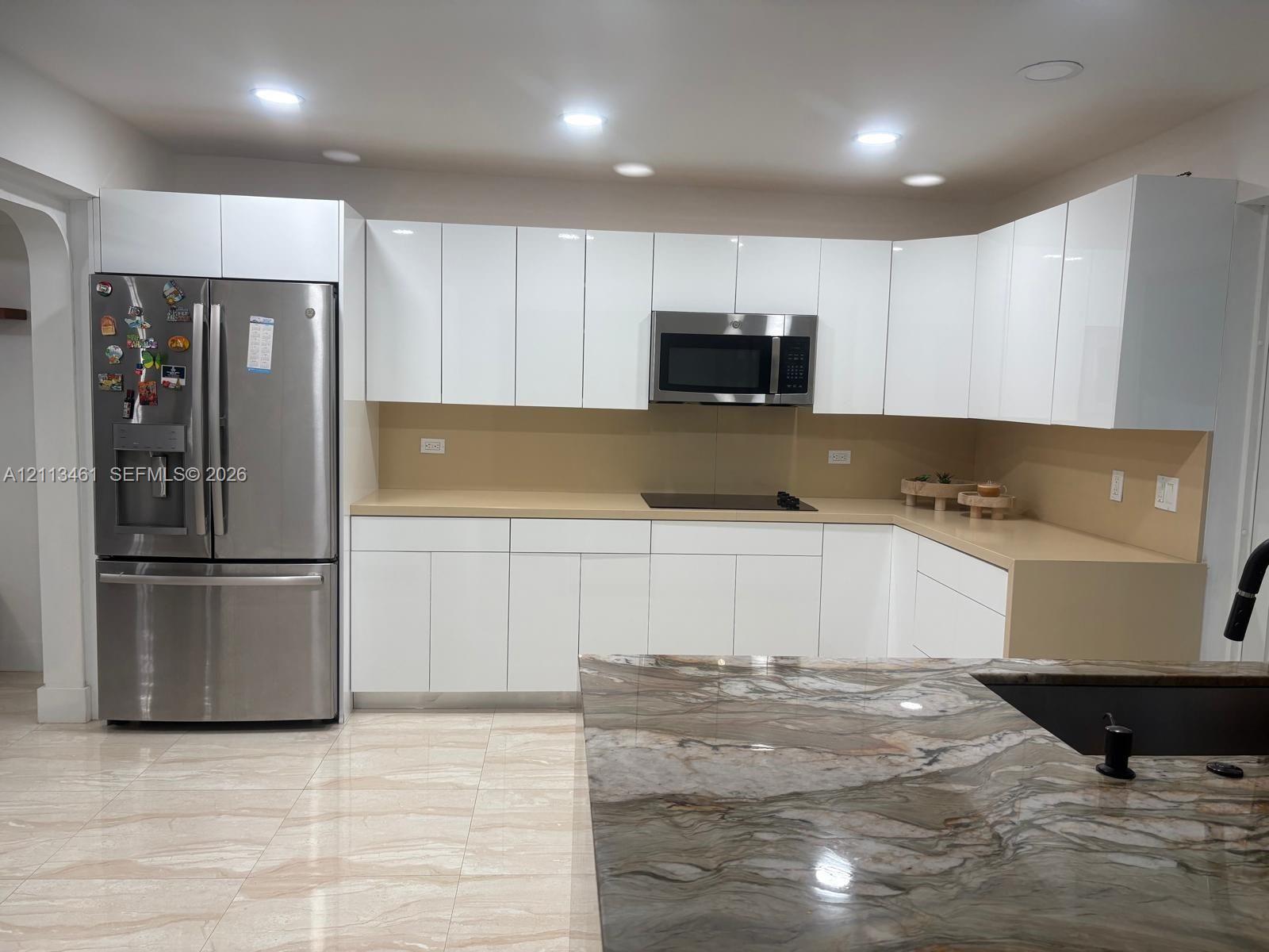 Kitchen featuring white high-gloss cabinetry, stone-finish countertops, stainless steel appliances, a center island with a stone countertop, and tile flooring