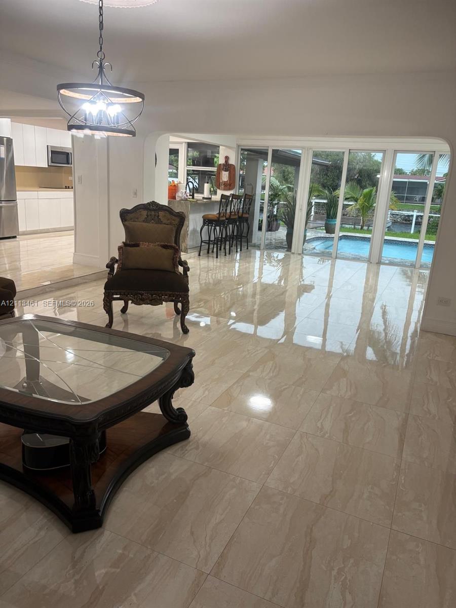 Open-concept living space featuring large-format tile flooring, a multi-panel sliding glass door, a built-in kitchen breakfast bar, and a decorative metal chandelier