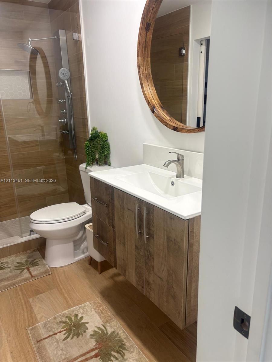 Floating vanity with wood-finish cabinetry, integrated white countertop, walk-in shower with wood-finish tile surround, and circular wall-mounted mirror
