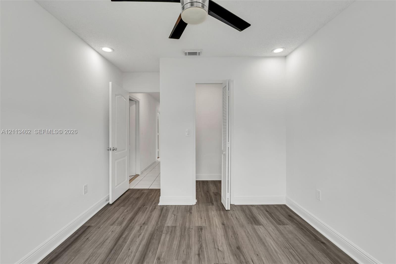 Wood-finish flooring, recessed lighting, ceiling fan with light fixture, louvered-door closet, and raised-panel interior door