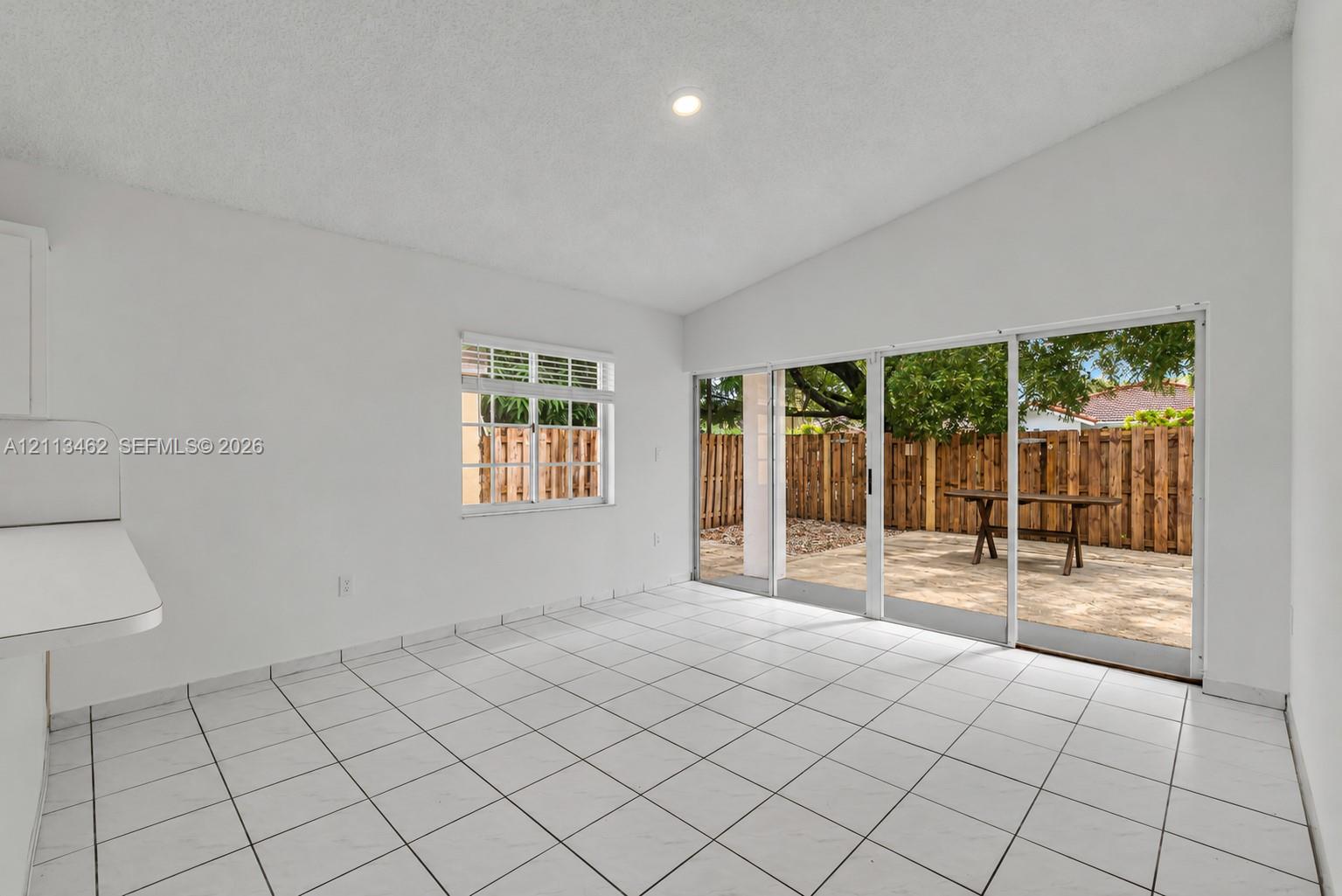 Room featuring white tile flooring, vaulted ceilings, recessed lighting, and large sliding glass doors providing outdoor access