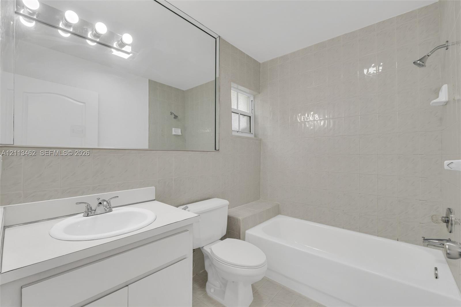 Bathroom featuring full-wall vanity mirror, white cabinet with integrated countertop sink, wall-mounted light fixture, and tile-surround shower and tub combination