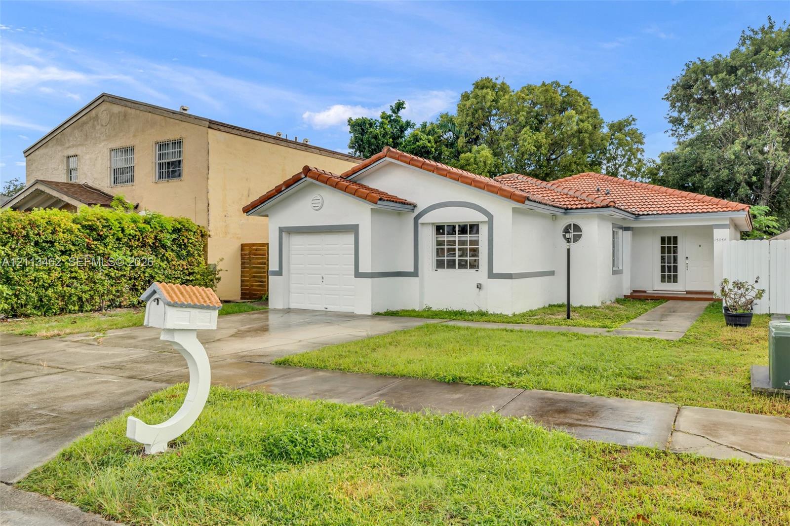 Stucco exterior featuring a terracotta tile roof, attached single-car garage, and custom curved mailbox