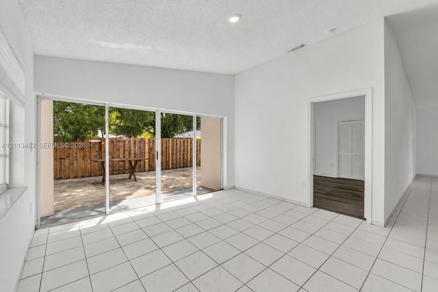 Open-concept room featuring white ceramic tile flooring, vaulted ceilings, recessed lighting, and multi-panel sliding glass doors providing access to a paved patio