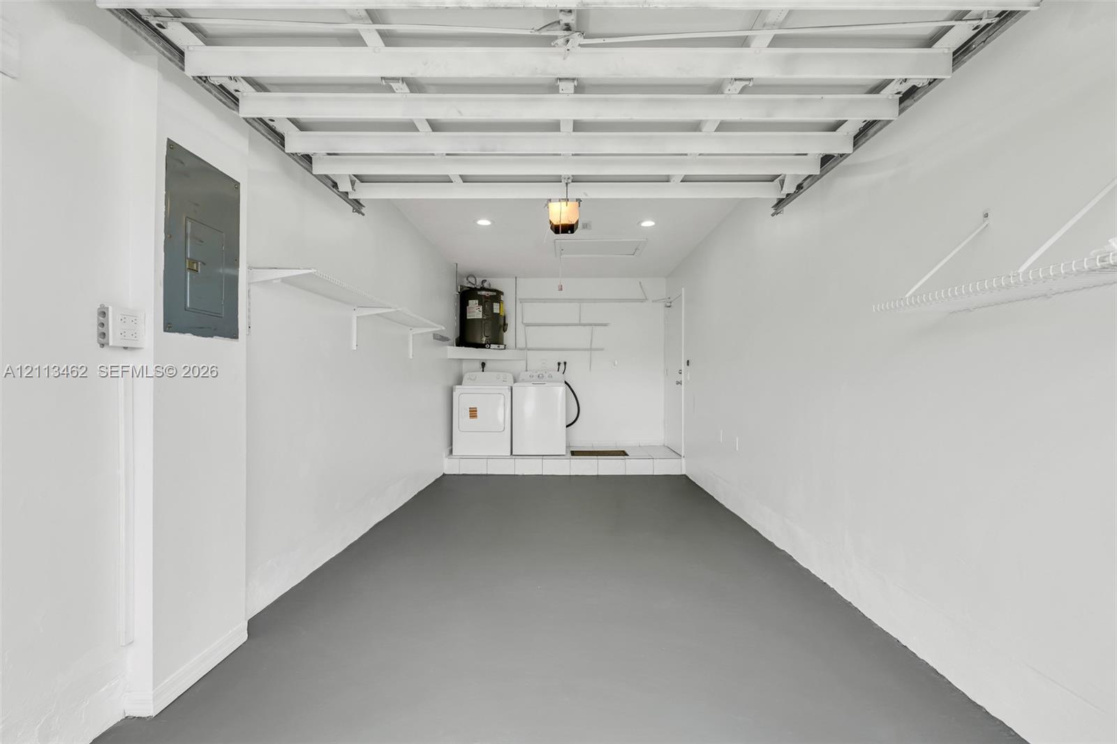 Finished interior space featuring epoxy-coated flooring, white walls, integrated wall-mounted shelving, recessed lighting, and a dedicated laundry area with water heater