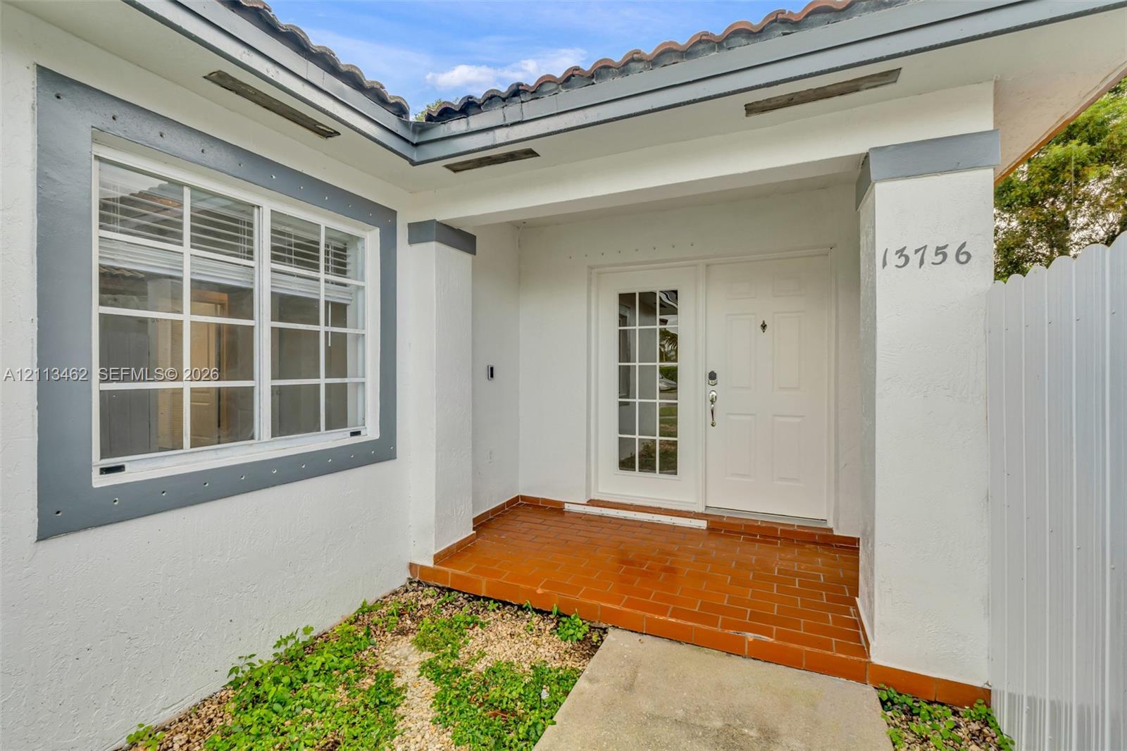 Covered entryway featuring a terracotta tile floor, stucco exterior, multi-pane front door, and a multi-pane window with contrasting trim