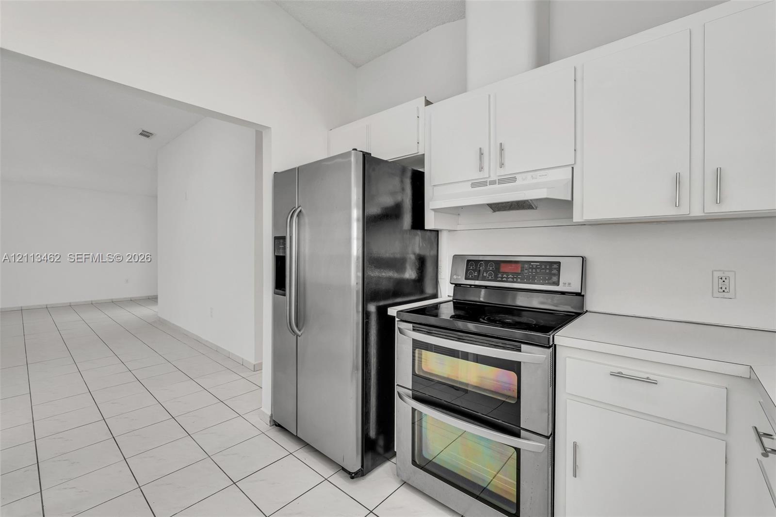 Kitchen featuring white cabinetry, stainless steel double-oven range, stainless steel refrigerator, and tile flooring