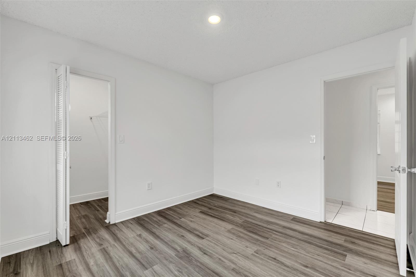 Interior space featuring neutral wall paint, wood-finish flooring, a recessed ceiling light, and louvered closet doors