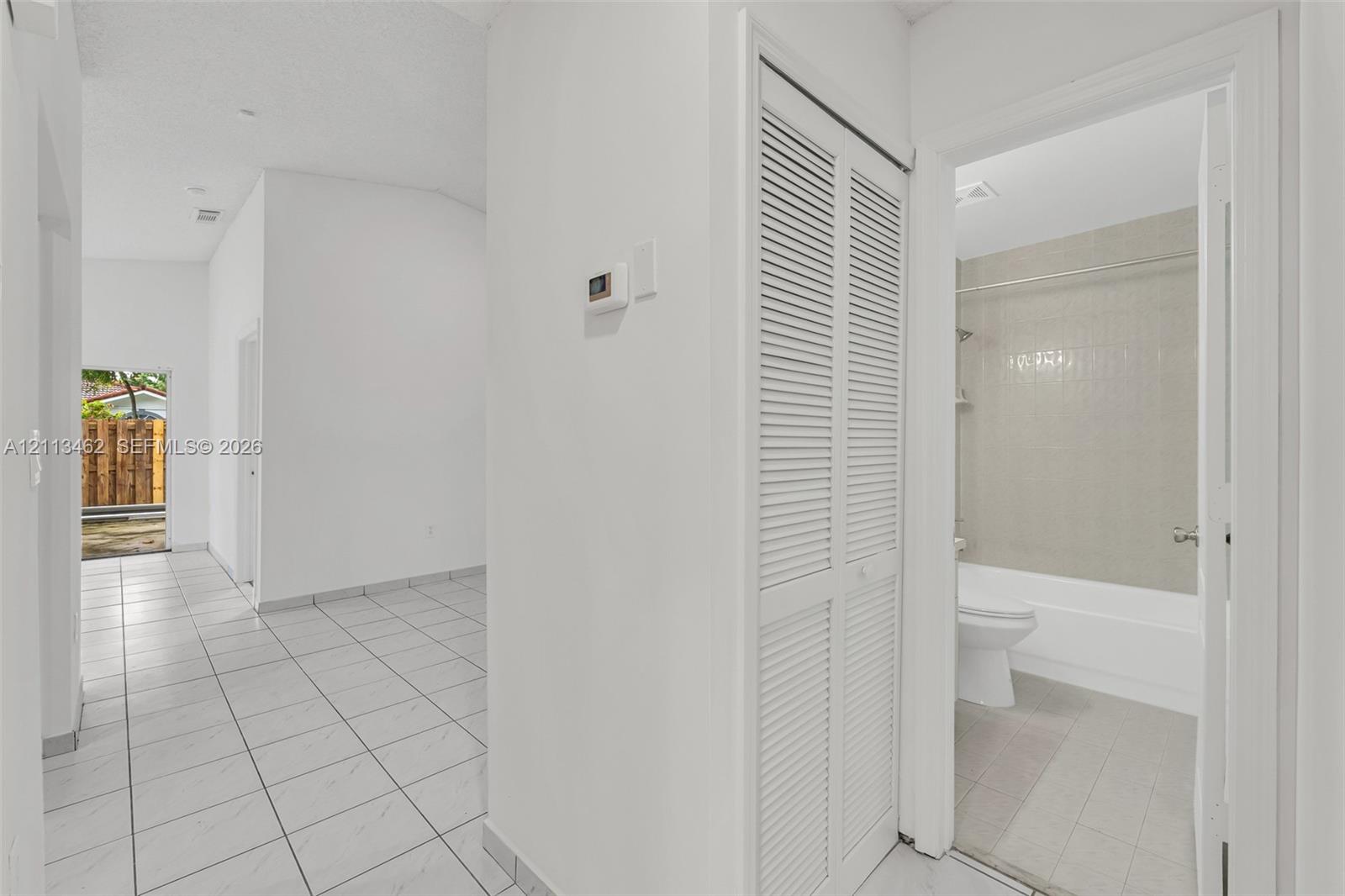Interior space featuring white tile flooring, louvered bi-fold closet doors, and a bathroom equipped with a tub-shower combination