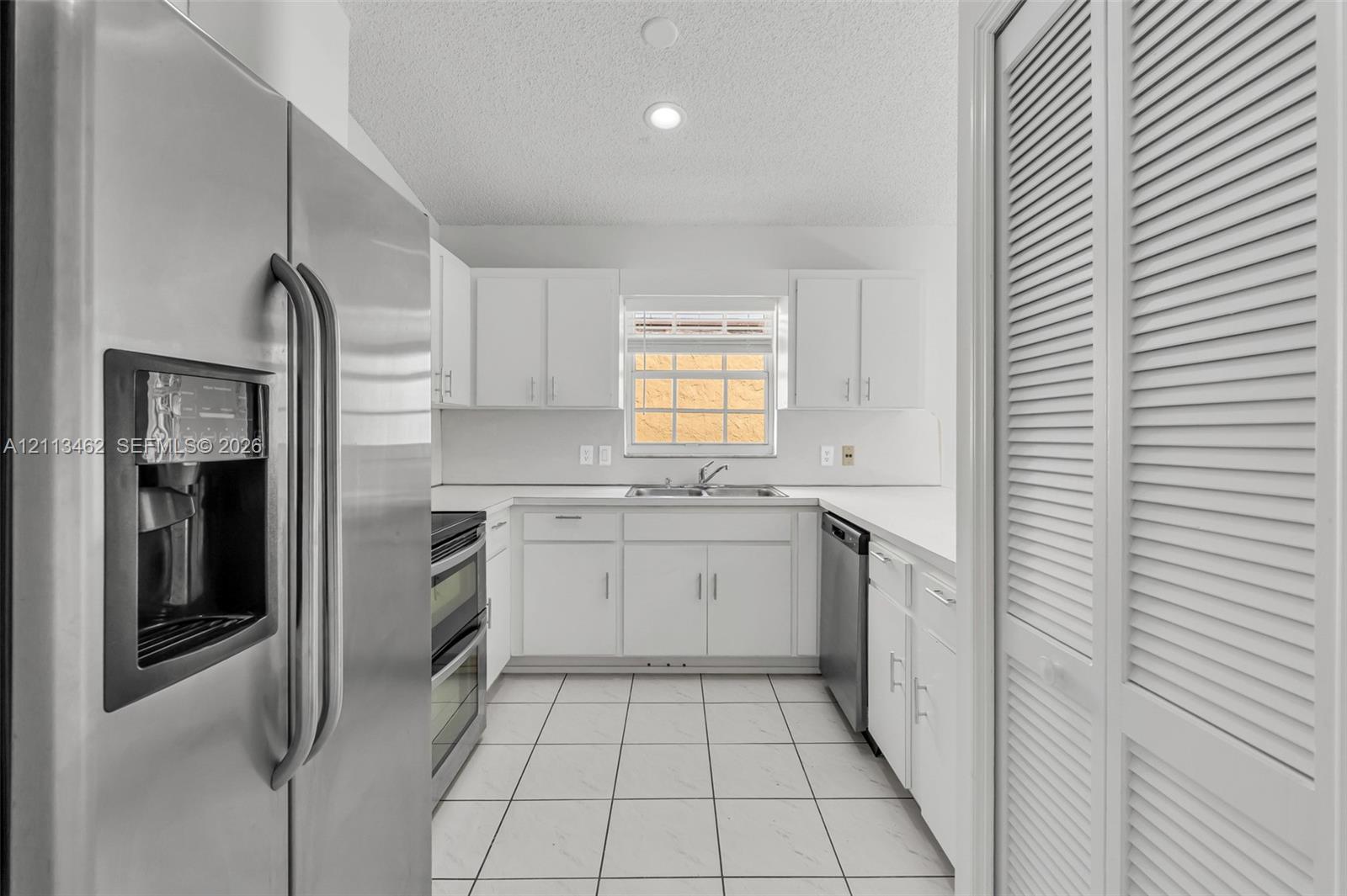 Kitchen featuring stainless steel appliances, white cabinetry, solid-surface countertops, tile flooring, and louvered closet doors
