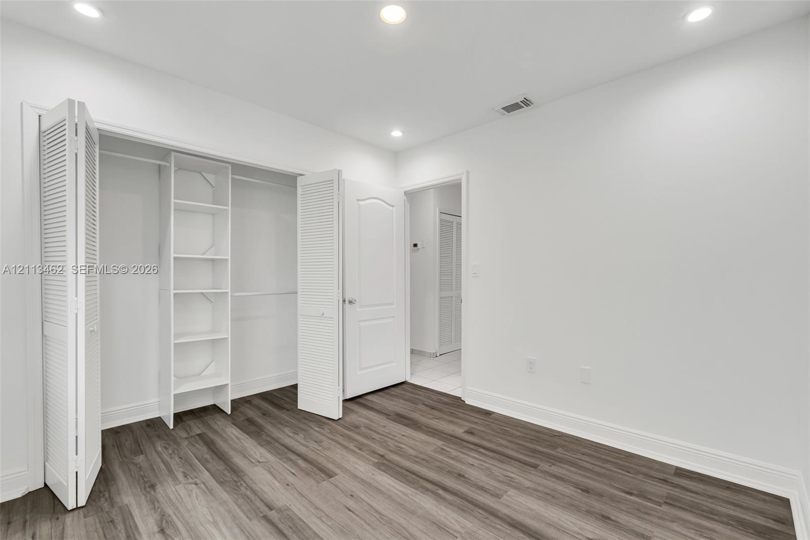 Wood-finish flooring, recessed lighting, and a reach-in closet with integrated shelving and louvered bifold doors