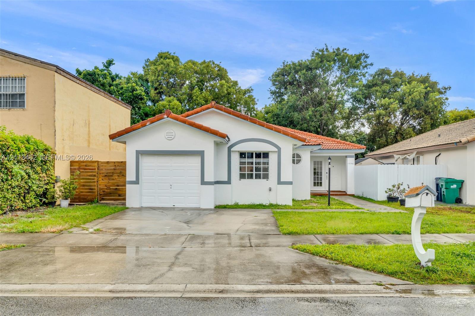 Single-story stucco exterior featuring a red tile roof, attached one-car garage, grid-pane windows, and concrete driveway