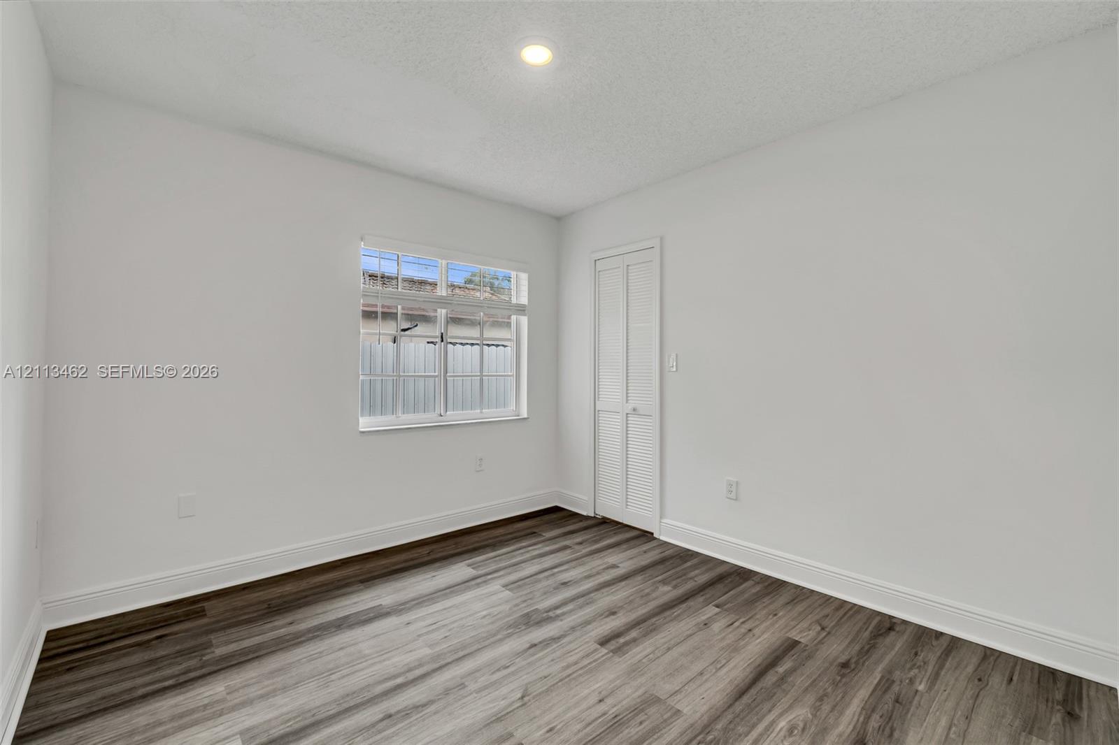 Room featuring wood-finish flooring, recessed lighting, and a multi-pane window, complete with a closet featuring bifold louvered doors