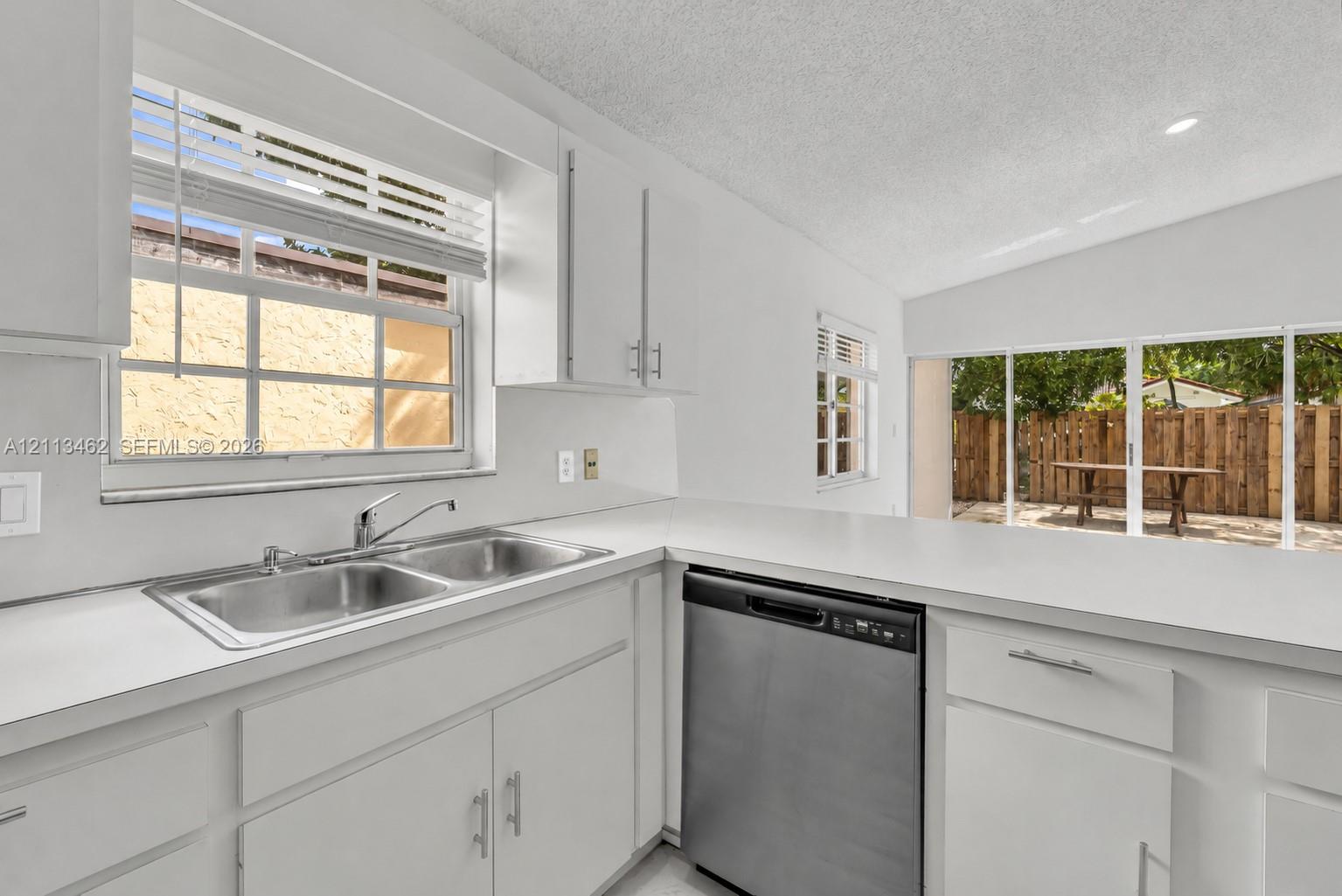 Kitchen featuring white cabinetry, solid surface countertops, a stainless steel dual-basin sink with a chrome faucet, a stainless steel dishwasher, and sliding glass doors