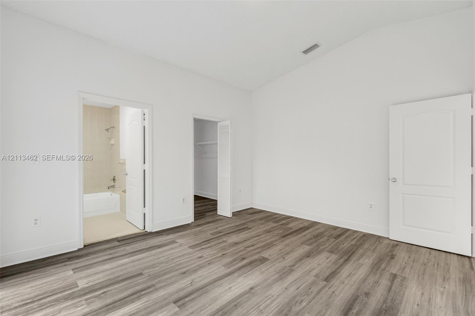 Room featuring a vaulted ceiling, wood-finish flooring, and two panel doors leading to a bathroom and closet