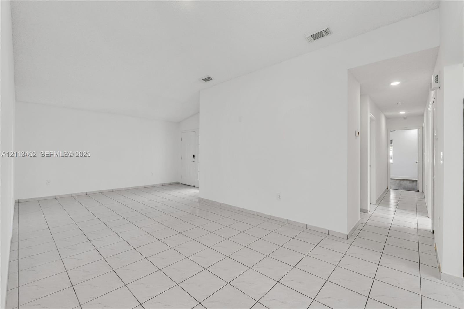 Open interior area featuring vaulted ceilings, neutral wall finishes, and light-toned tile flooring throughout