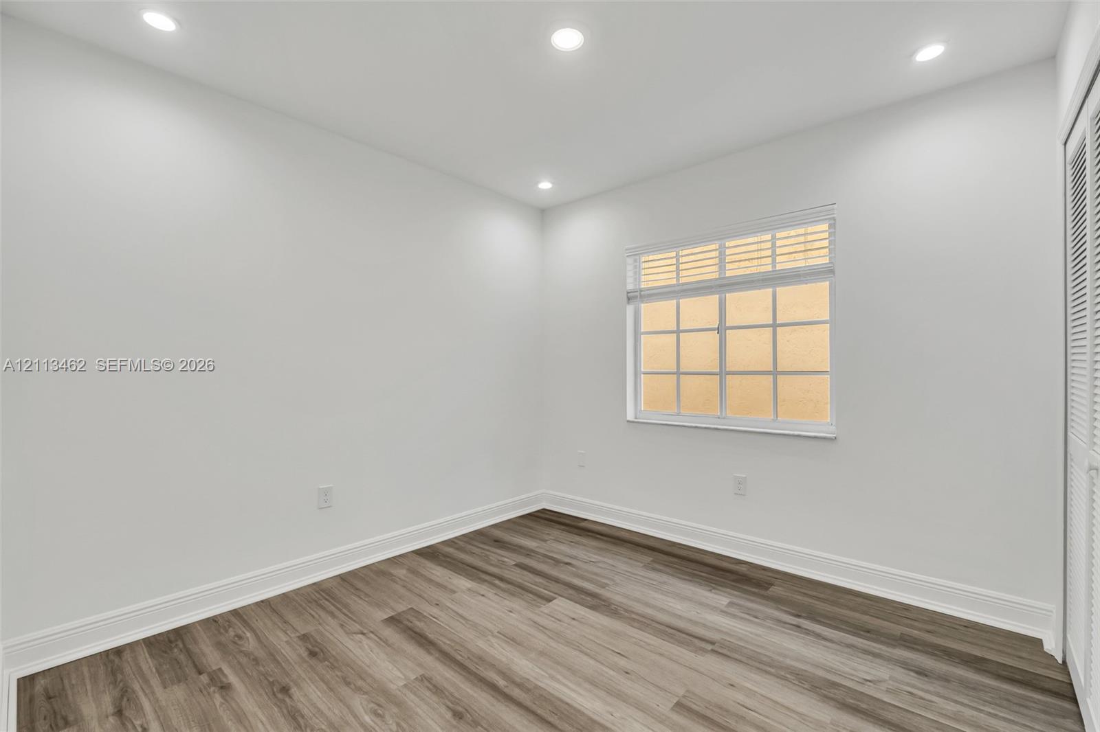 Neutral interior featuring wood-finish flooring, recessed lighting, and a multi-pane window with louvered blinds