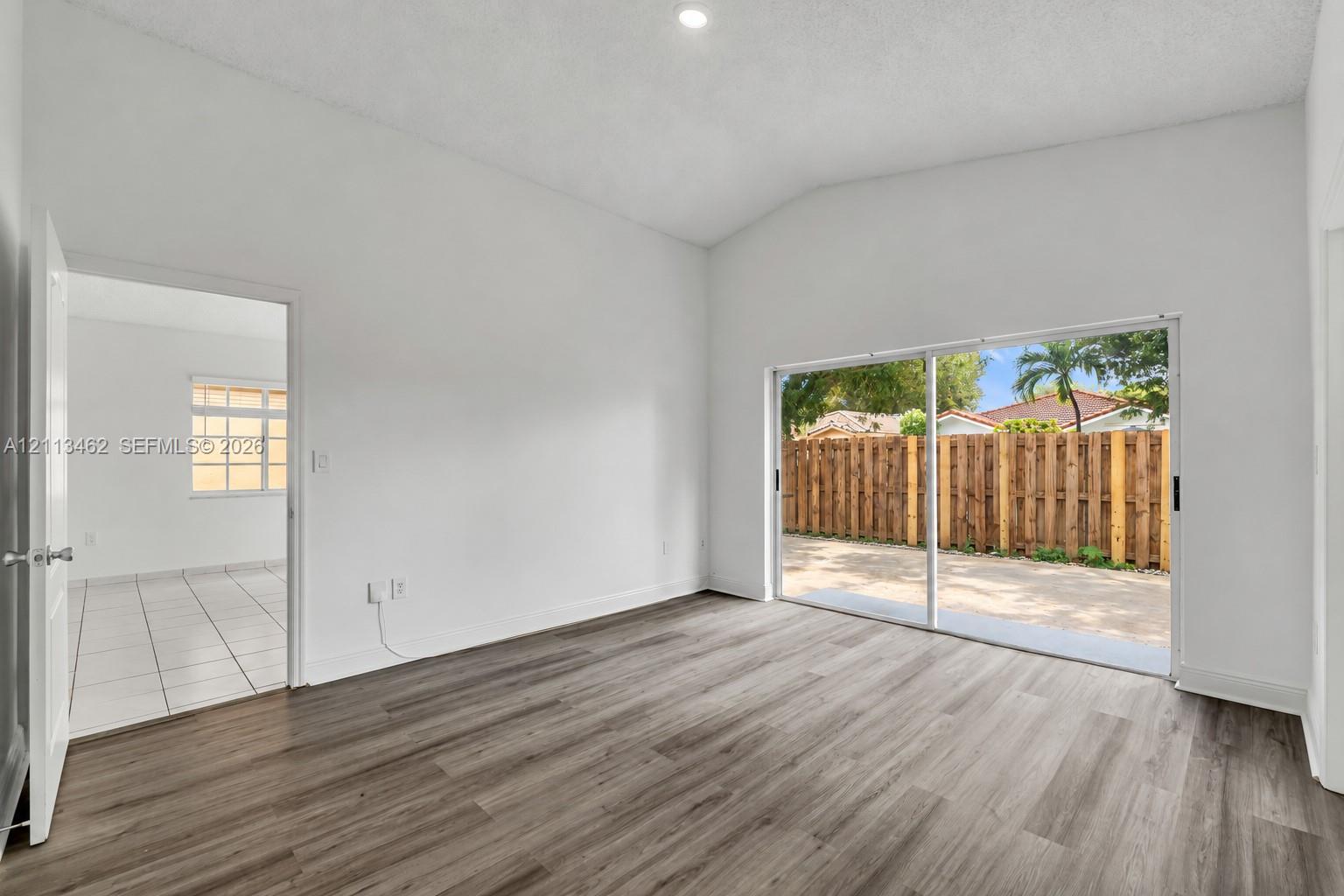Vaulted ceilings, wood-finish flooring, recessed lighting, and sliding glass doors with access to an exterior patio