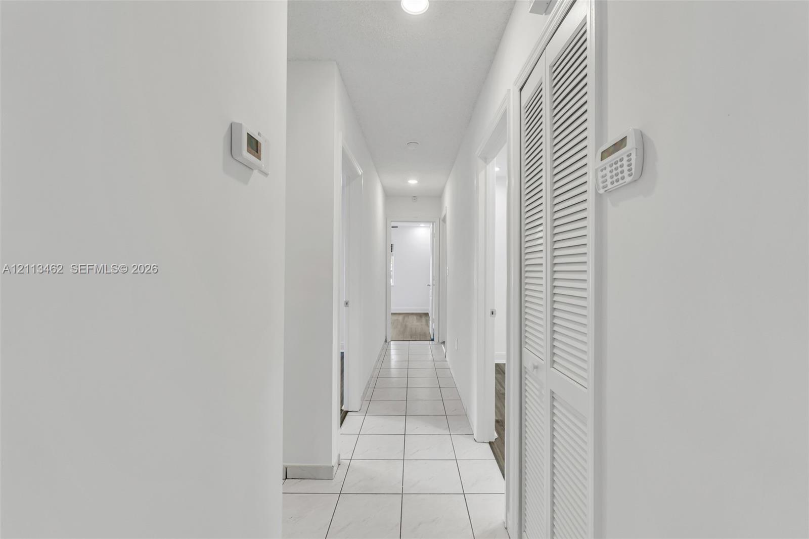 Hallway featuring white ceramic tile flooring, recessed lighting, and louvered bi-fold closet doors