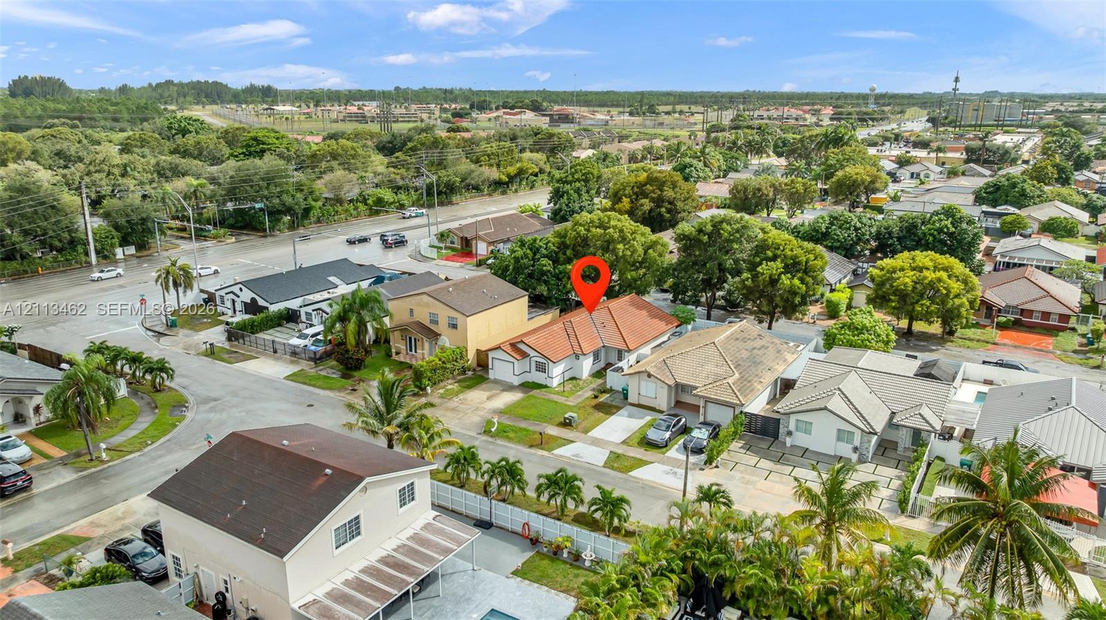 Aerial perspective of a single-story residence featuring a terracotta-style tile roof, stucco exterior, concrete driveway, and mature landscaping