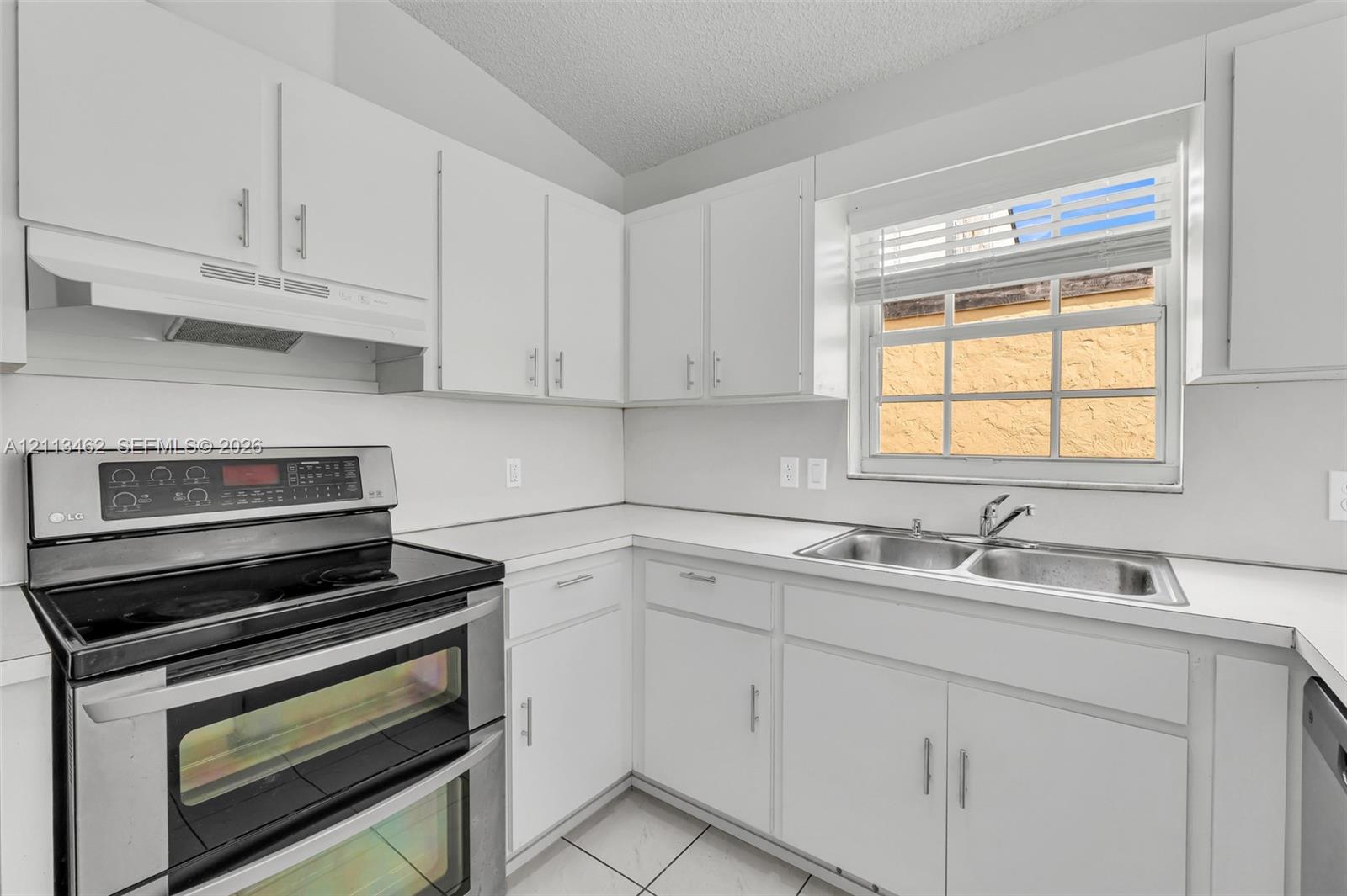 Kitchen featuring white cabinetry, solid-surface countertops, stainless steel double-oven range, integrated range hood, and double-basin stainless steel sink