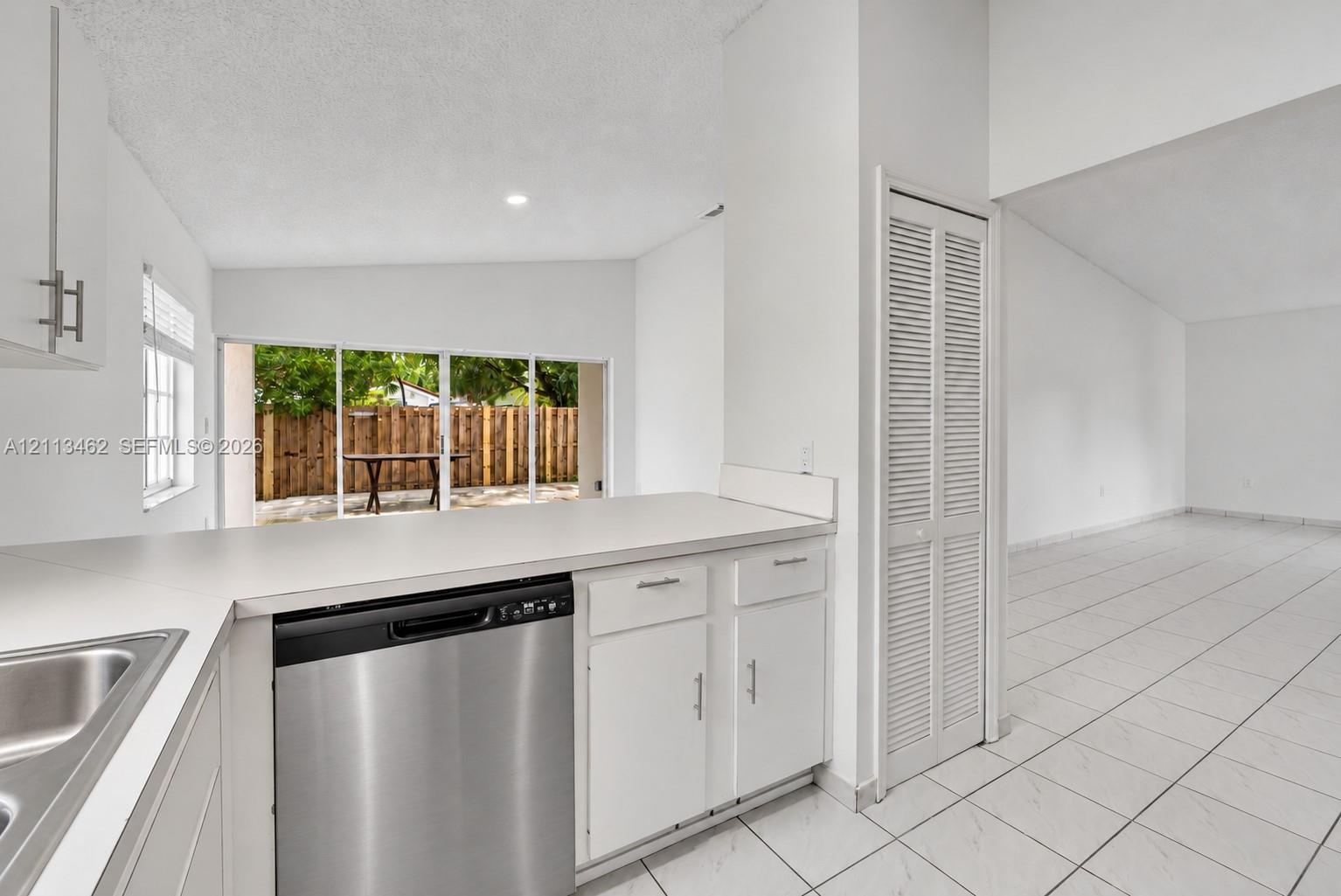Kitchen featuring white cabinetry, stainless steel dishwasher, solid-surface countertops, floor-to-ceiling louvered-door closet, and neutral tile flooring